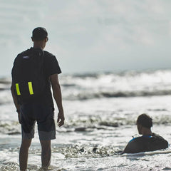 Person with GORUCK backpack in water, rucking on the beach, another person sitting in surf