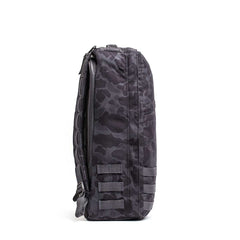 Side view of the GR1 rucksack in black and dark gray camo, featuring multiple straps and a zipper, designed to Special Forces-grade standards, shown on a white background.