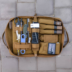 Open tan Pistol Rug with scissors, tools, tourniquets, and supplies neatly organized inside like a modular pistol case, shown on stone tiles.