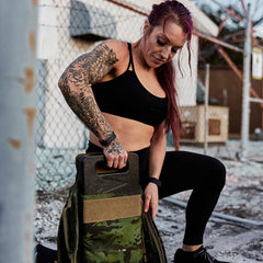 Woman inserts GORUCK ruck plate into camo backpack outdoors, rucking fitness gear