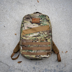 A camouflage Rucker 5.0 rucksack with lumbar support rests on a rough, gray concrete surface.