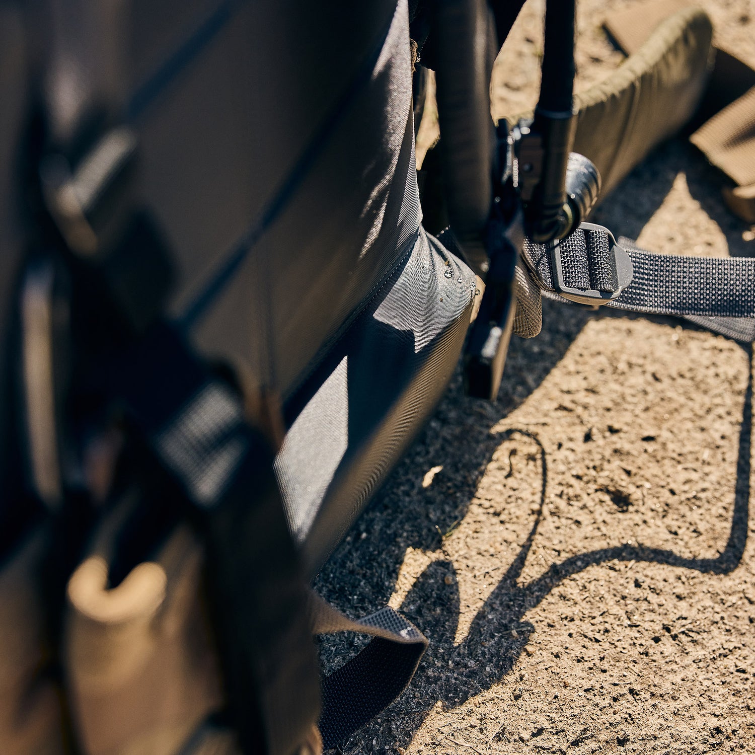Close-up of the Rucker 5.0’s black straps and tan fabric with lumbar support, resting on sunlit rough concrete.