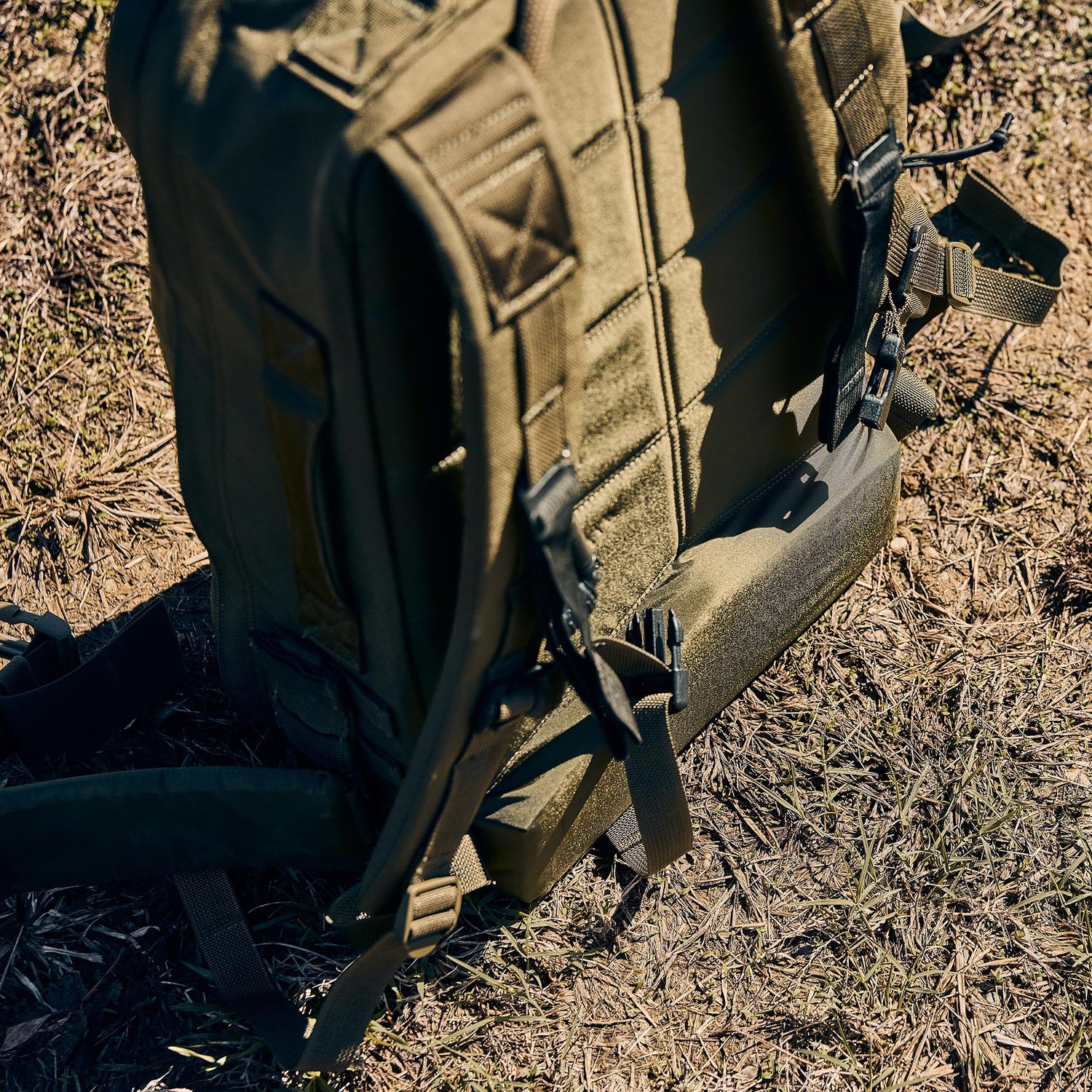 A close-up of the green Rucker 5.0 with straps and lumbar support, lying on dry grass outdoors—perfect for comfortable rucking adventures.
