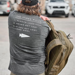 GORUCK Three Rules Tee charcoal shirt with printed rules, man holding rucksack outdoors