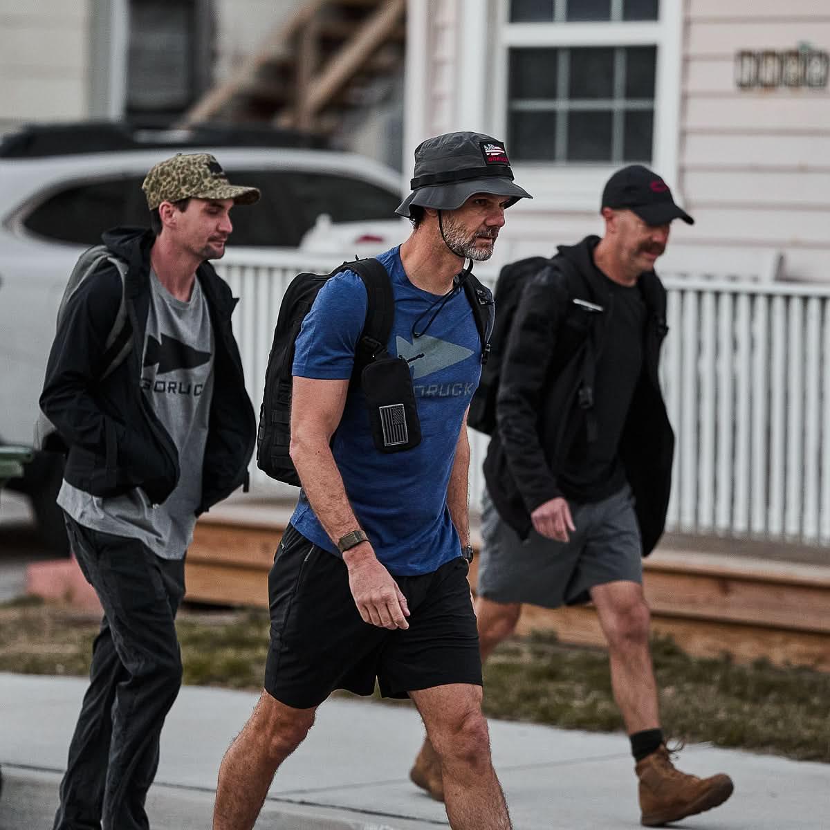 Three men rucking outdoors in GORUCK gear and navy tee, walking on a sidewalk