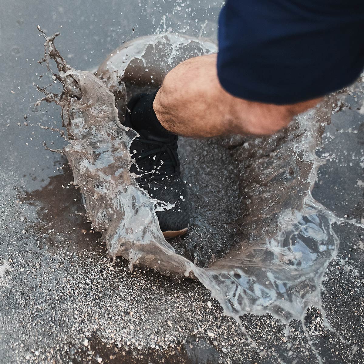 A person’s foot splashes in a muddy puddle, with water spraying up around a black sneaker.