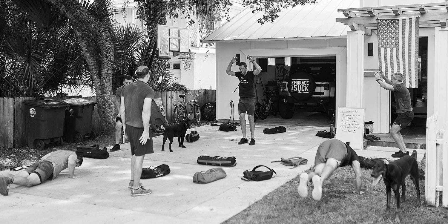 Five people and two dogs exercising outside a house, with workout gear and an American flag visible.