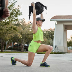 Woman in neon workout gear doing an overhead lunge with a GORUCK rucksack outdoors