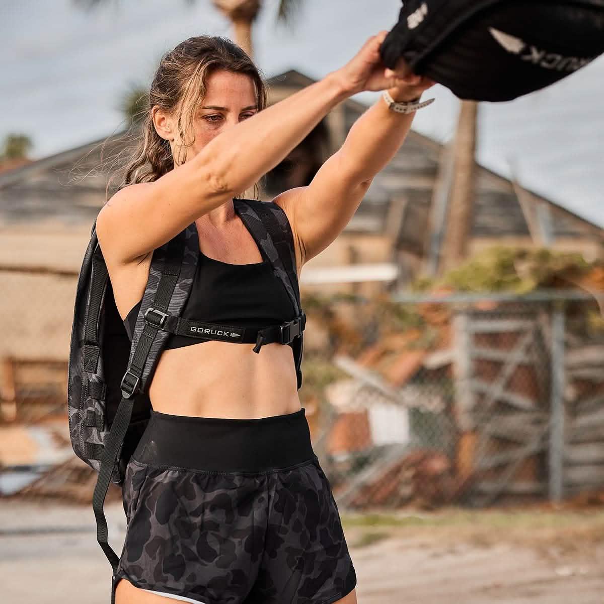 Woman rucking outdoors in GORUCK black camo shorts and rucksack, active fitness gear