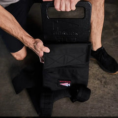 Man loading GORUCK 10LB ruck plate into a black GORUCK rucksack on concrete floor