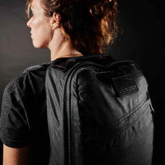 Woman wearing a black GORUCK backpack, rugged rucking gear, side view, dark background