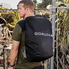 Man outdoors wearing black GORUCK backpack cover, rucking gear, chain link fence background