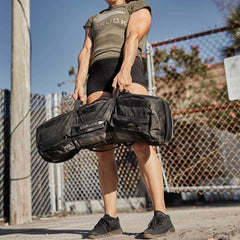 Athlete lifting GORUCK 80lb sandbag outdoors, showcasing durable rucking gear