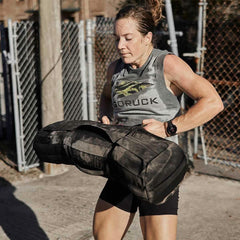 Athlete lifting GORUCK sandbag outdoors, wearing GORUCK tank and fitness watch