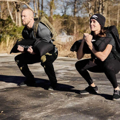 Two people doing outdoor squats with GORUCK sandbags and rucksacks