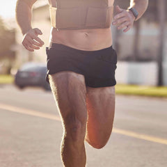 Man running outdoors in GORUCK Ranger Panties shorts and weighted vest on sunny street.