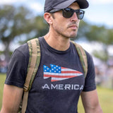 Man wearing GORUCK America shirt, camo rucksack, sunglasses, and cap outdoors