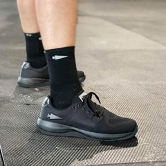 GORUCK Ballistic trainers in black with reflective logo, worn on gym floor, close-up view.