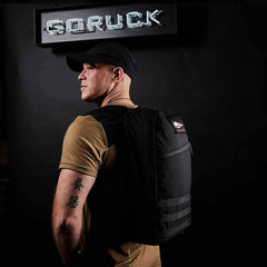 Man wearing a GORUCK black rucksack backpack, standing under GORUCK sign