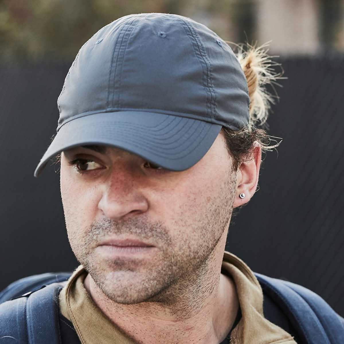 Man in charcoal GORUCK cap and backpack, outdoor urban setting, rugged rucking gear style