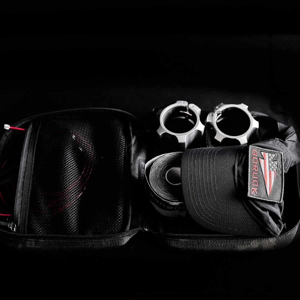 GORUCK rucking gear kit with black GORUCK cap, roll of tape, metal clamps, and mesh pouch