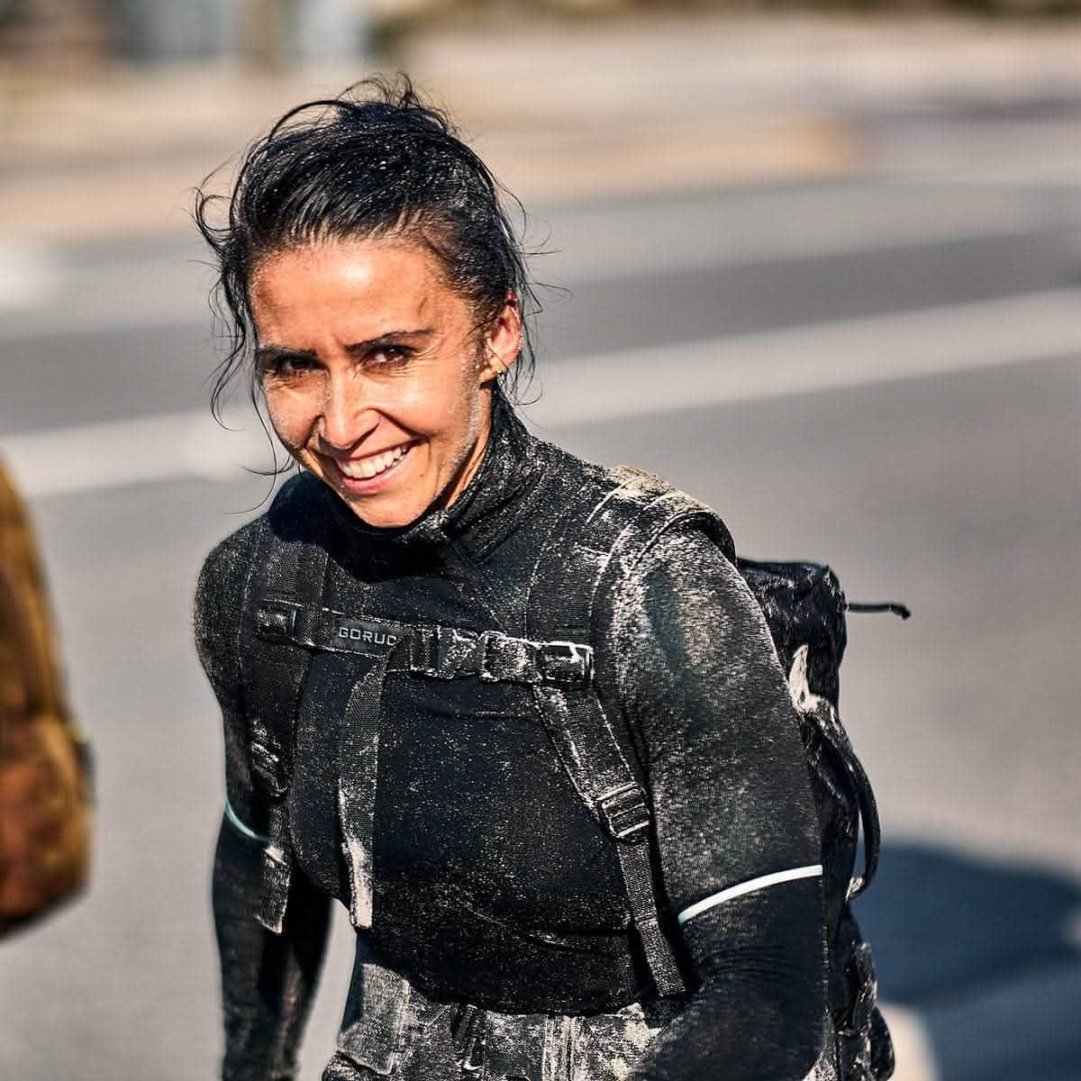 Woman smiling outdoors, wearing GORUCK gear and a sandy sternum strap backpack