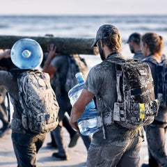 GORUCK rucking gear in use by group on sandy beach, participants carrying heavy loads