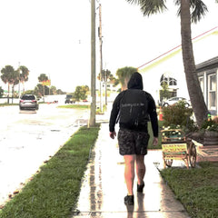Person rucking in rain with GORUCK black rain cover on backpack, walking on wet sidewalk
