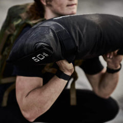 Athlete performing squat with GORUCK 60 lb sandbag, wearing tactical rucking gear