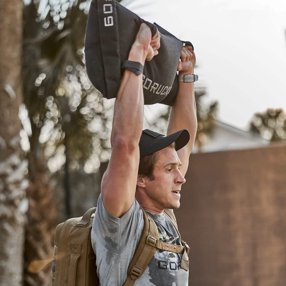 Man lifting GORUCK sandbag overhead outdoors, wearing rucksack and GORUCK gear