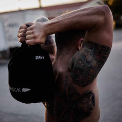 Tattooed man lifting GORUCK 26 lb ruck sandbag outdoors during rucking workout