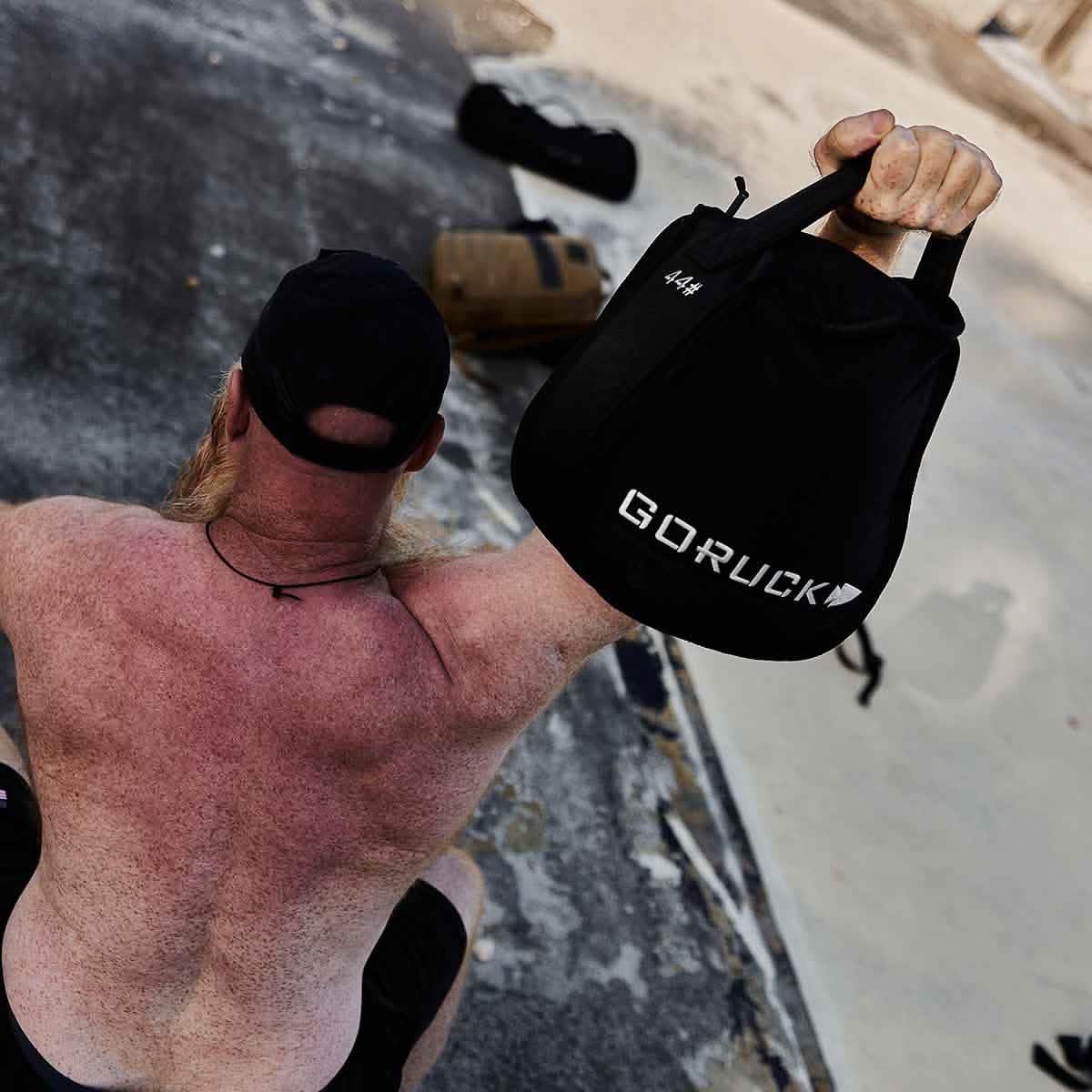 Man lifting GORUCK 44 lb sandbag outdoors, showcasing durable rucking gear
