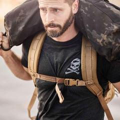 GORUCK athlete wearing black Tribe Tee with skull logo, carrying sandbag and rucking backpack outdoors