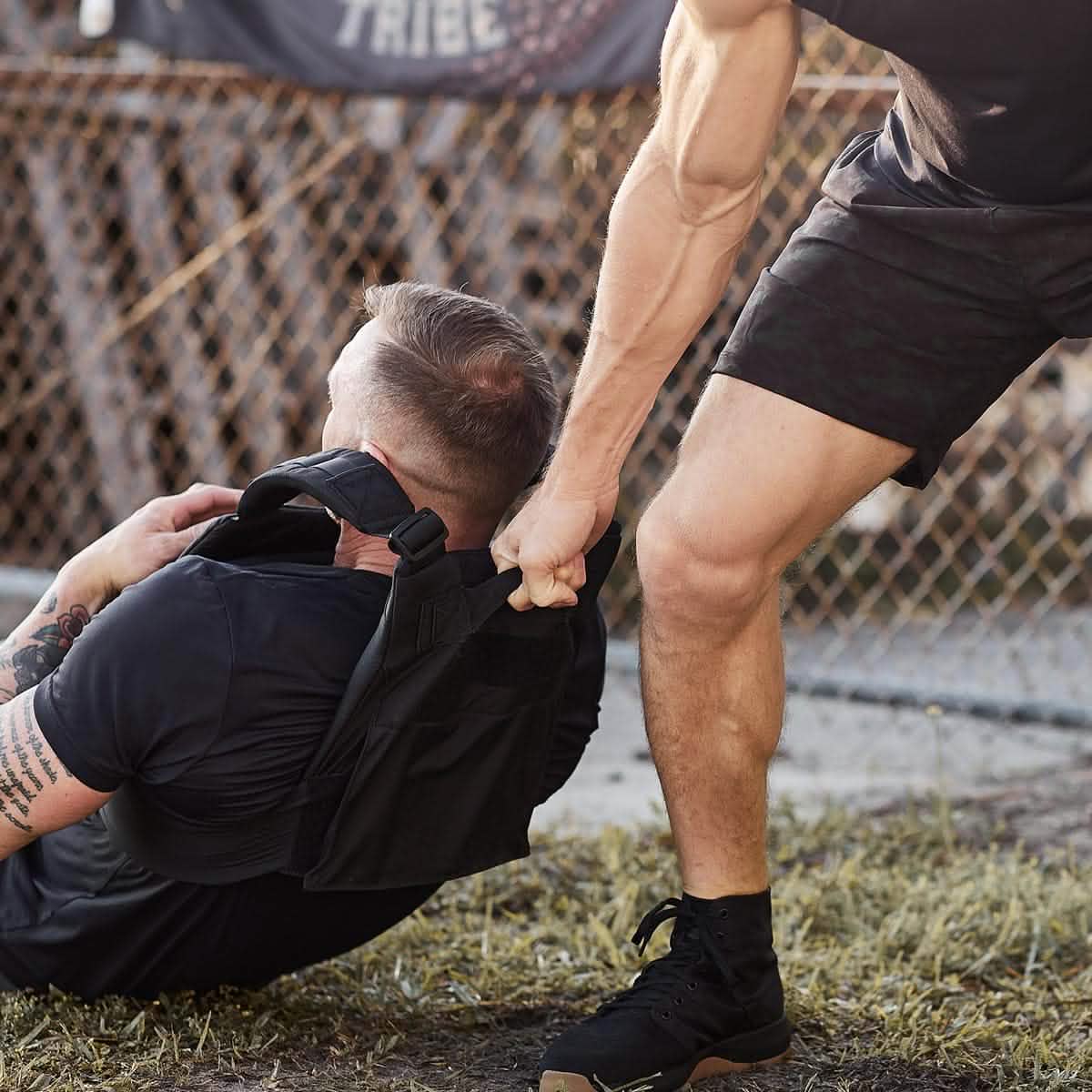 A man pulls another man's back while he wears the Training Weight Vest - Black.